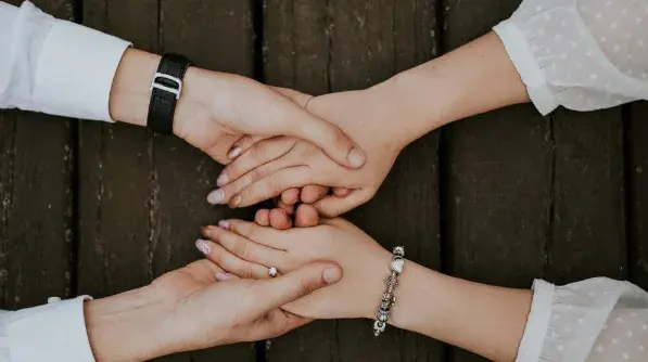 Two pairs of hands clasped together in mutual support