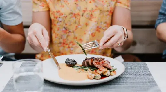 A meal at a table — hands using a fork and knife to cut into food