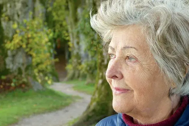 An older woman smiling outdoors with a thoughtful expression