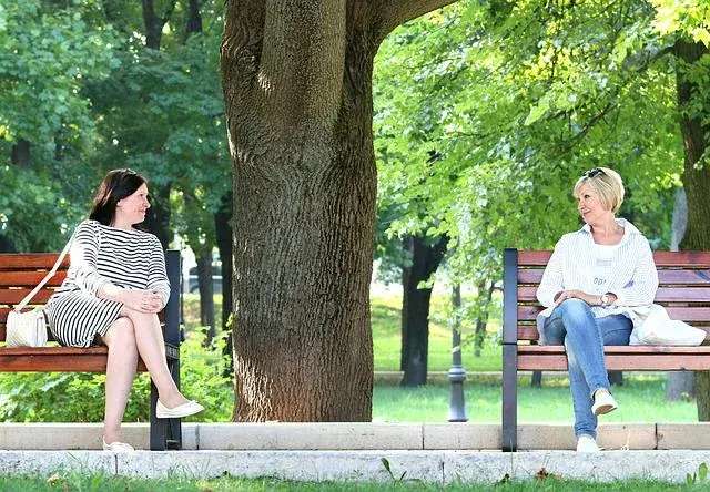 Two women seated on a park bench in summer, in conversation